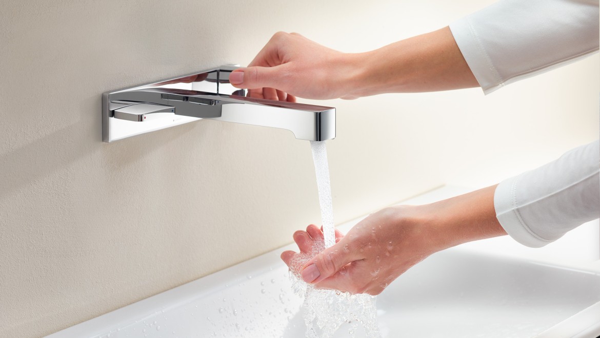 Woman turns on the tap and feels the water strength and temperature (© Geberit)